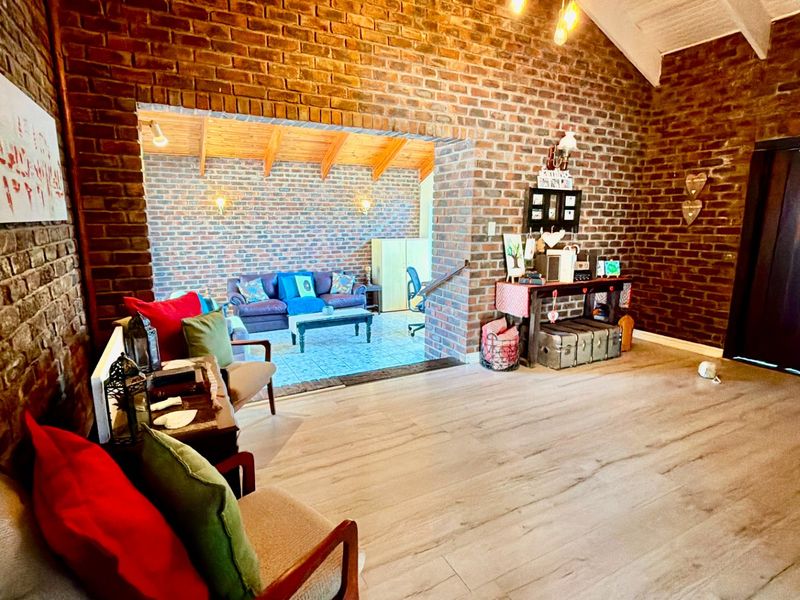 Spacious open-plan living area featuring rustic exposed brick walls, vaulted timber ceilings with exposed beams, and modern laminate flooring.