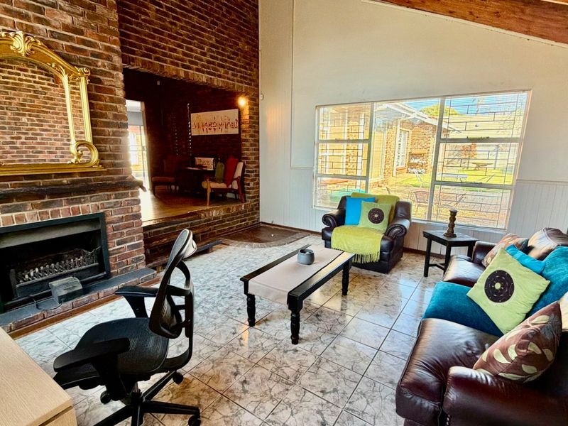 Spacious living room featuring a prominent brick fireplace, tiled flooring, and large windows that provide ample natural light and views of the garden.