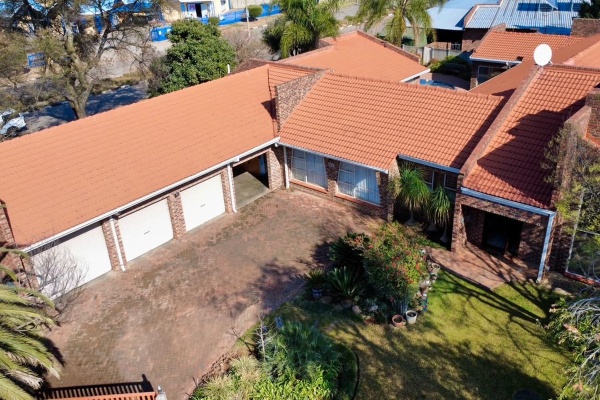 Aerial view of a brick-faced house featuring a triple garage, tiled roof, and a well-maintained front garden with a paved driveway.