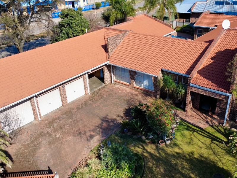 Aerial view of a brick-faced house featuring a triple garage, tiled roof, and a well-maintained front garden with a paved driveway.