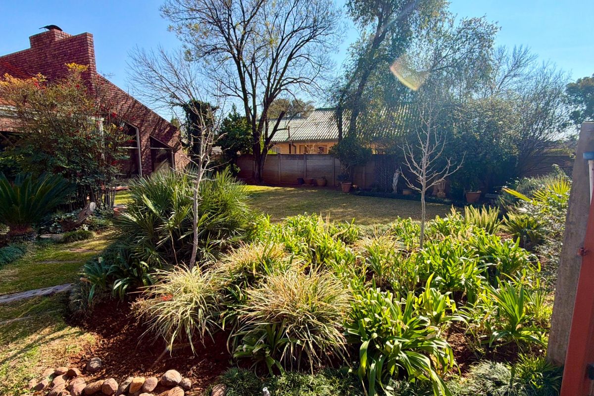 A spacious rear garden featuring established landscaping, a lawn area, and a view of the brick-clad house exterior with a prominent chimney.
