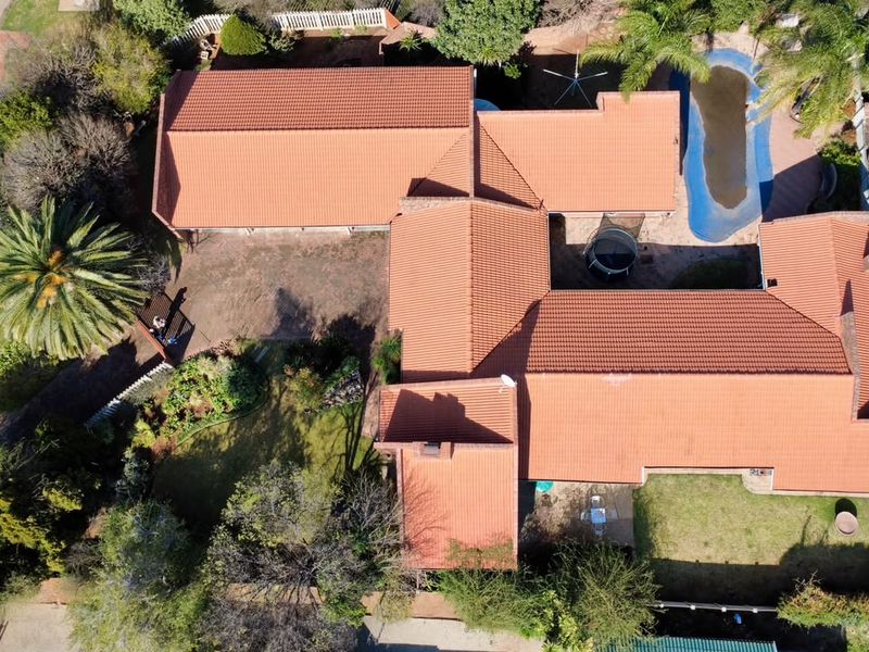 Aerial view of a residential property featuring a tiled roof, swimming pool, landscaped garden, and paved driveway area.