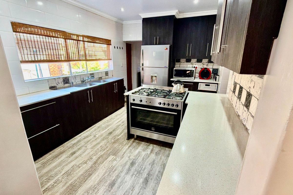 Modern kitchen featuring dark wood cabinetry, stone countertops, a gas stove with oven, and a double sink with tiled backsplash.