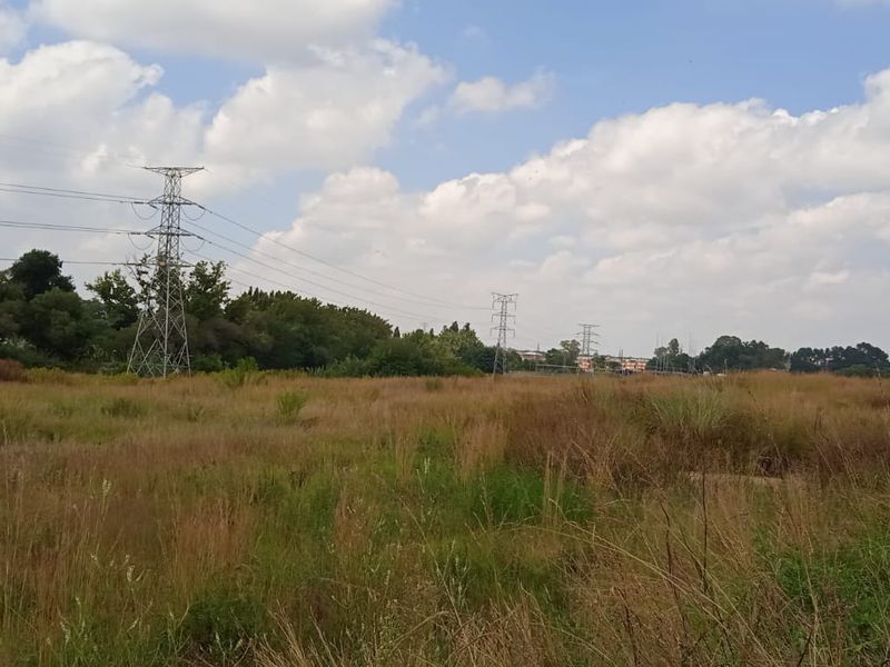 A wide, undeveloped residential land plot featuring natural grass cover and visible high-voltage transmission infrastructure.