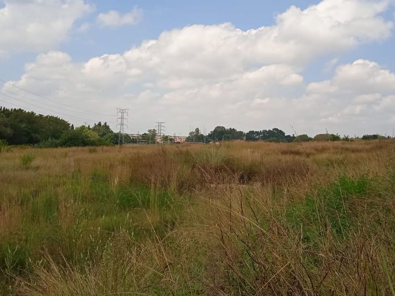 A view of a vacant residential plot featuring natural grass cover and visible electricity pylons in the background.
