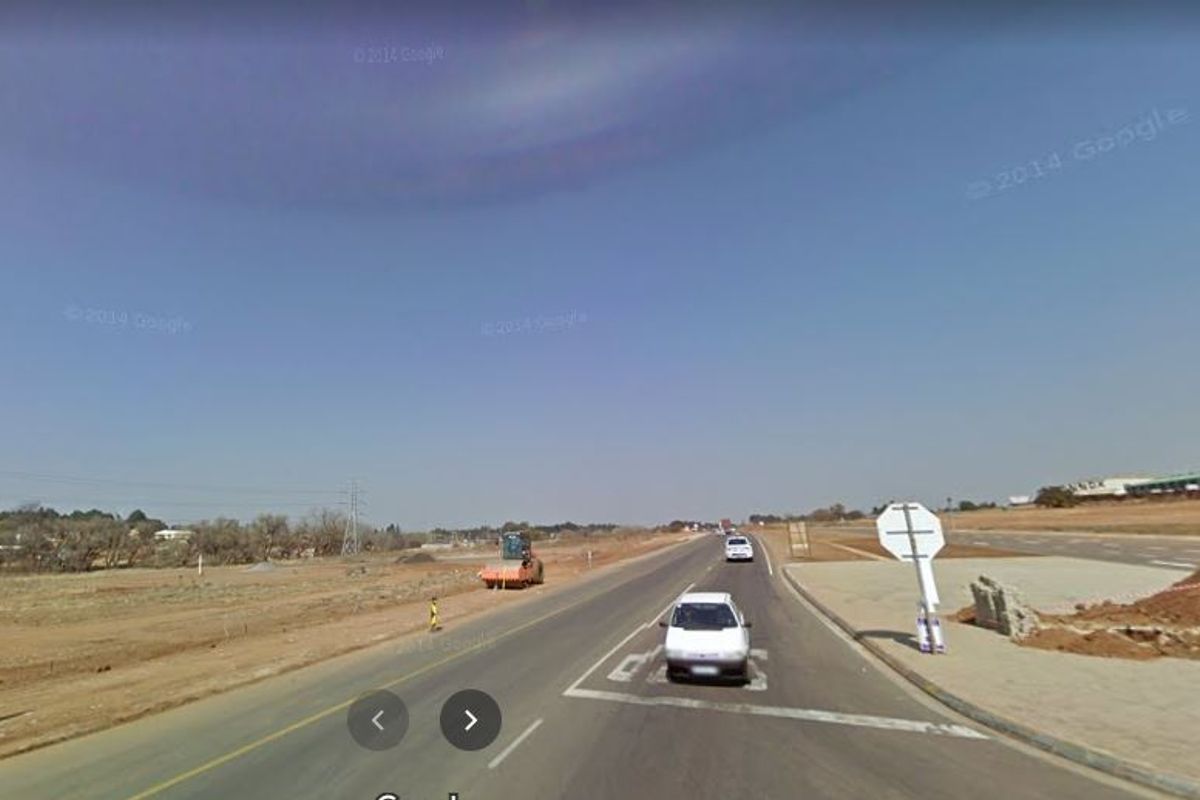 A street-level view of a paved road and surrounding vacant land area, showing local infrastructure and road signage.