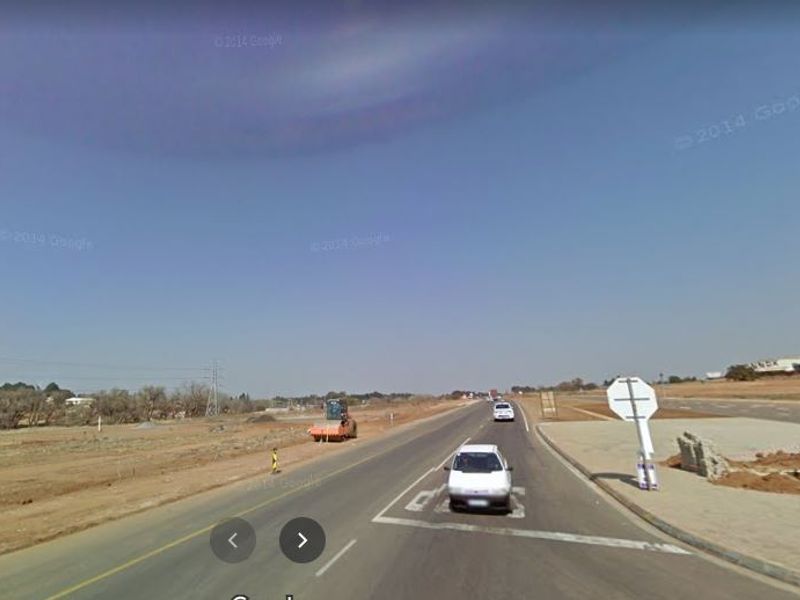 A street-level view of a paved road and surrounding vacant land area, showing local infrastructure and road signage.