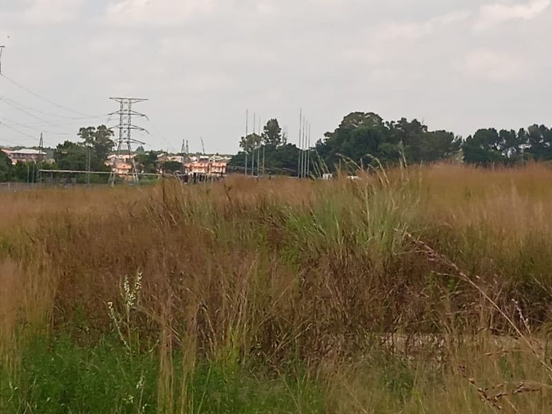 A view of a vacant residential plot featuring natural grass coverage and visible high-voltage power lines in the background.