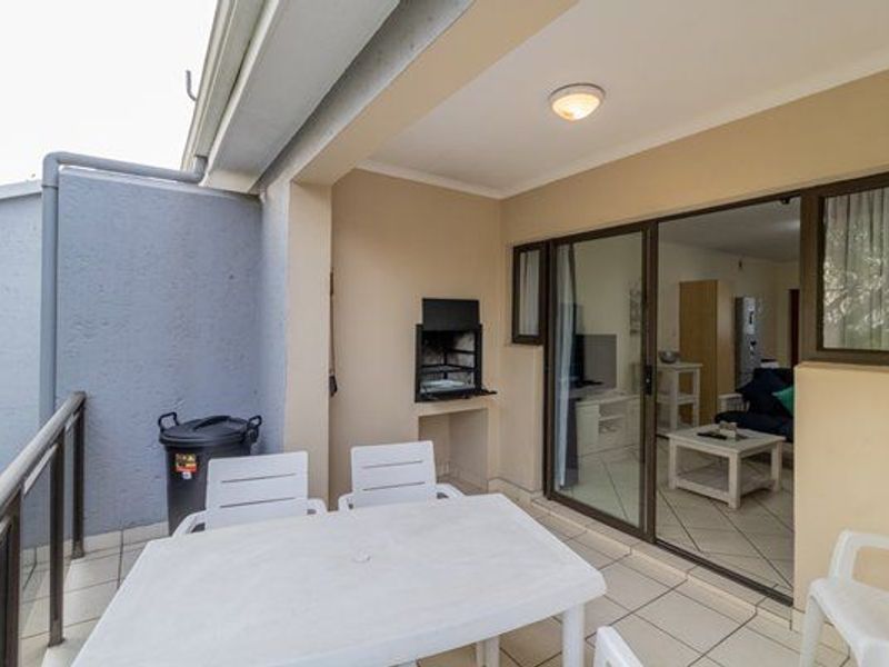 Covered balcony featuring a built-in braai, tiled flooring, and sliding door access to the interior living area.