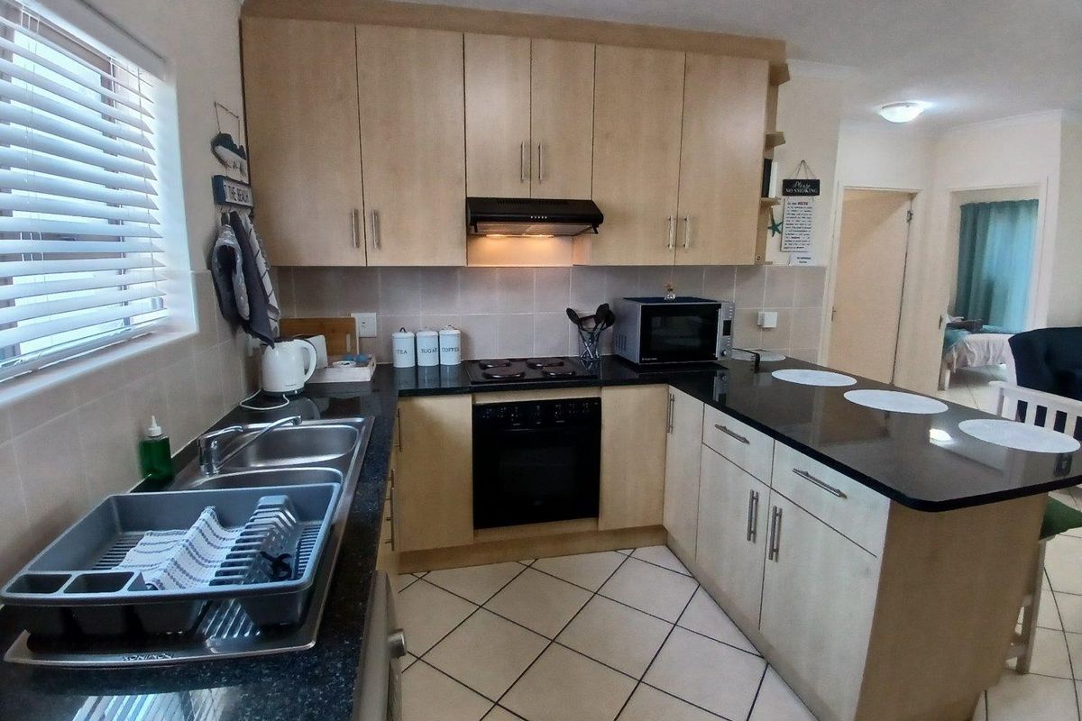 A functional kitchen featuring light wood cabinetry, dark granite countertops, a built-in oven with hob, and tiled flooring.