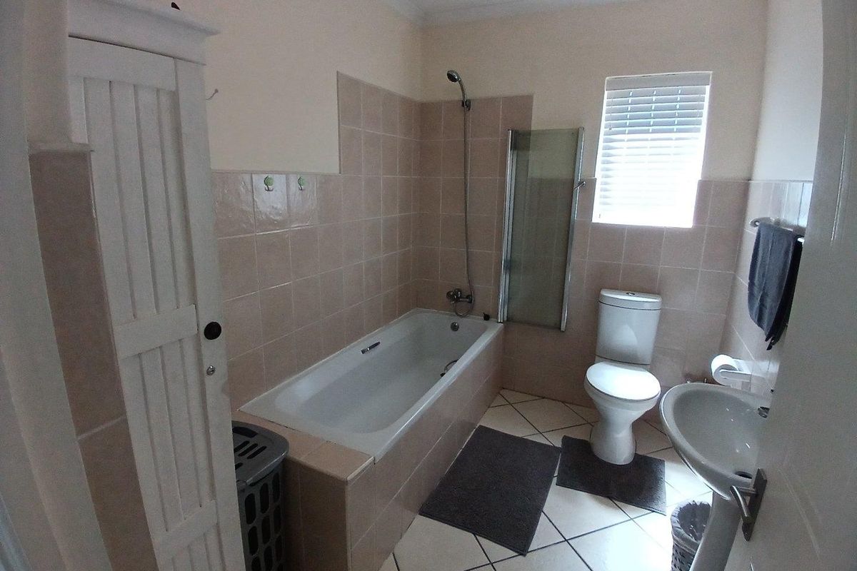 A functional bathroom featuring a bathtub with a shower attachment, glass screen, pedestal sink, and toilet with neutral wall and floor tiling.