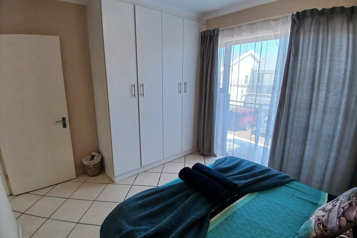 A bright bedroom featuring built-in cupboards, tiled flooring, and a sliding glass door providing direct access to a balcony.