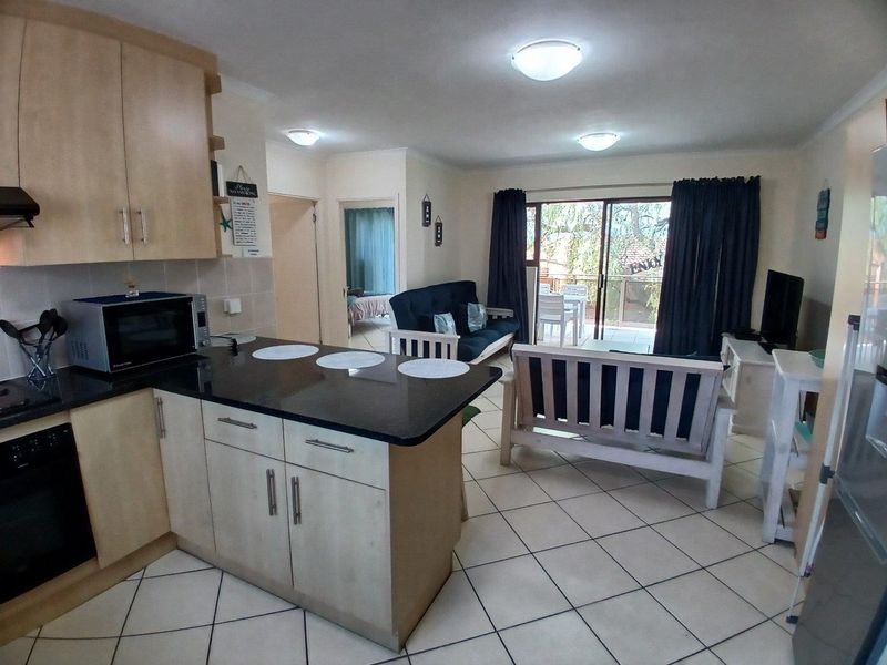 Open-plan living area featuring a functional kitchen with granite countertops, tiled flooring throughout, and direct access to a private balcony through sliding glass doors.