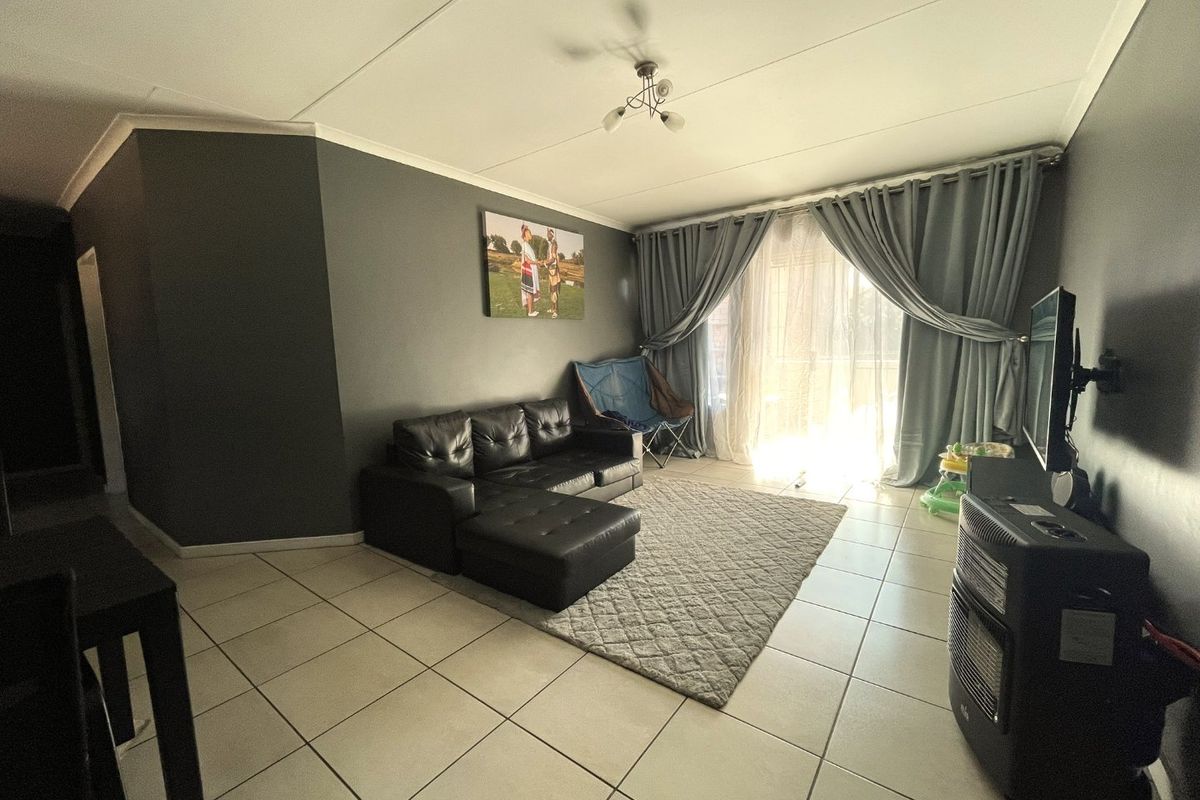 A living room featuring tiled flooring and a large sliding glass door that provides access to an outdoor area, allowing for natural light.