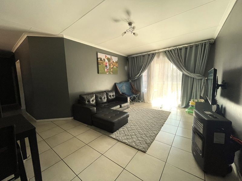 A living room featuring tiled flooring and a large sliding glass door that provides access to an outdoor area, allowing for natural light.
