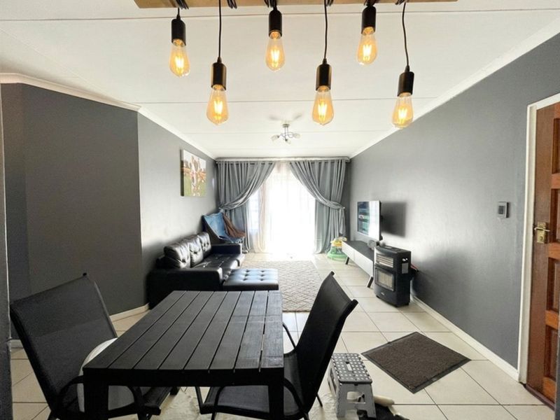 A living room featuring tiled flooring, modern pendant lighting, and a sliding glass door leading to an outdoor area.