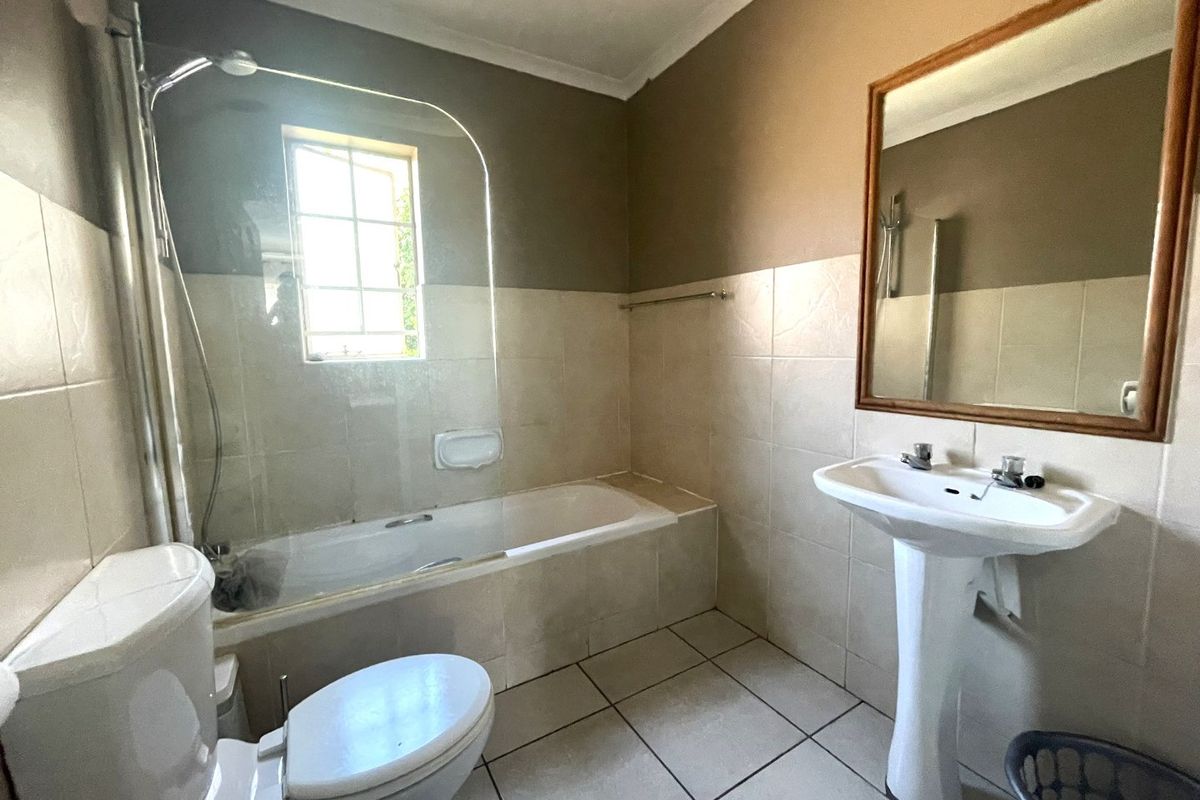 A functional bathroom featuring a pedestal basin, bathtub with a glass shower screen, and tiled finishes throughout.
