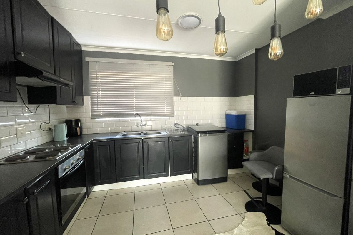 A modern kitchen featuring dark cabinetry, subway tile backsplash, stainless steel sink, and integrated electric hob and oven with tiled flooring.