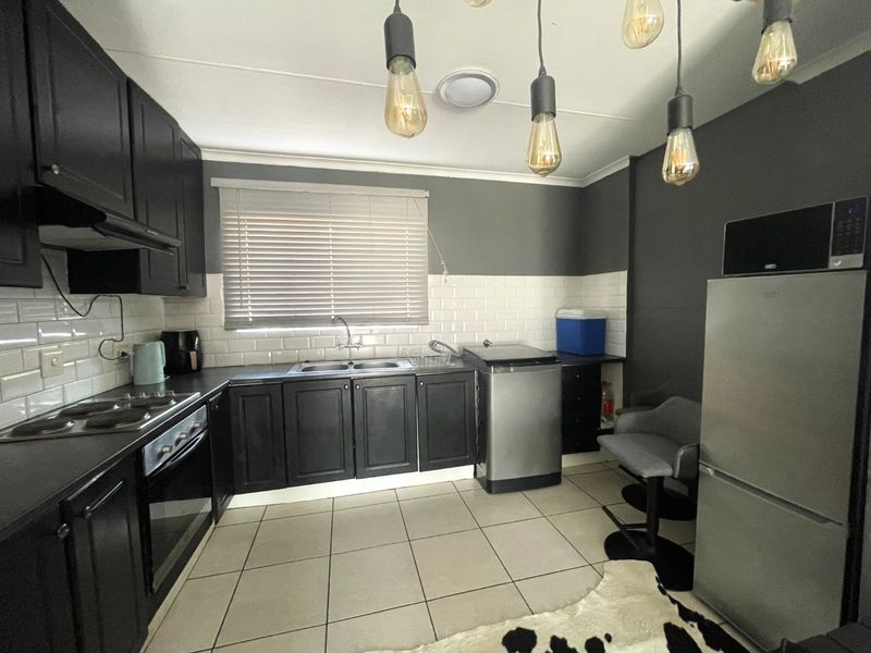 A modern kitchen featuring dark cabinetry, subway tile backsplash, stainless steel sink, and integrated electric hob and oven with tiled flooring.