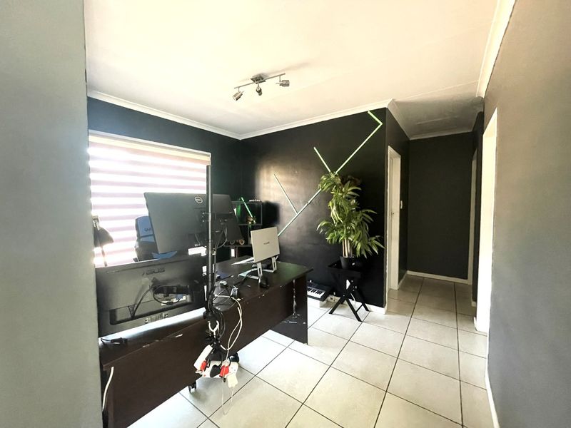 A functional office space featuring tiled flooring, track lighting, and roller blinds, currently utilized as a workspace.