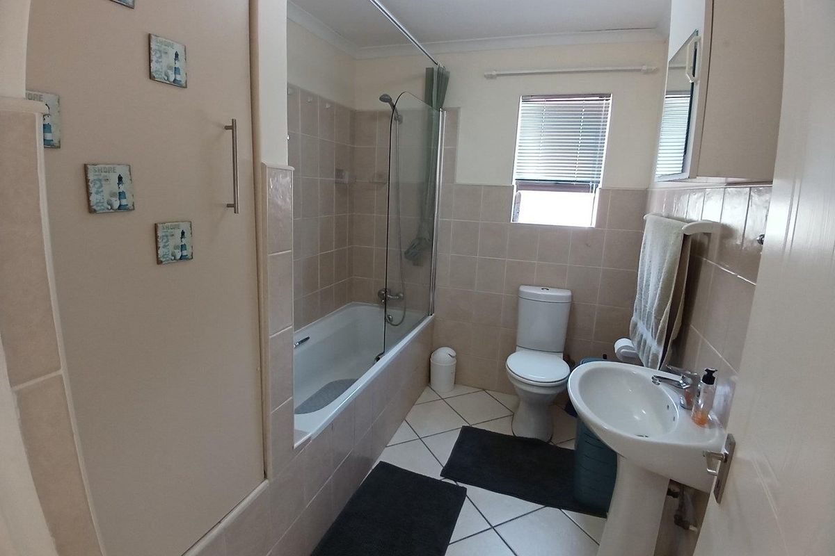 A functional bathroom featuring a bathtub with a glass shower screen, pedestal basin, and toilet, finished with neutral wall and floor tiles.