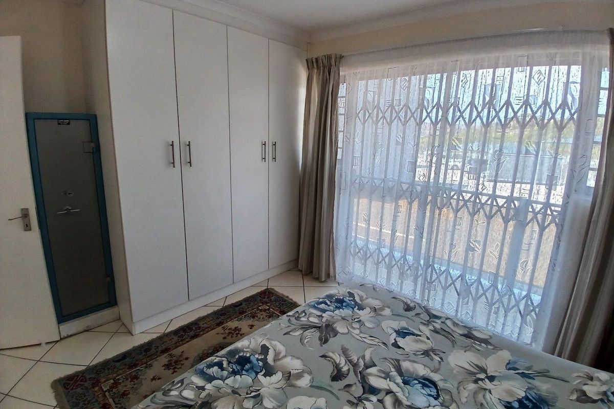 A bedroom featuring built-in cupboards, tiled flooring, and a sliding door with a security gate leading to an outdoor area.