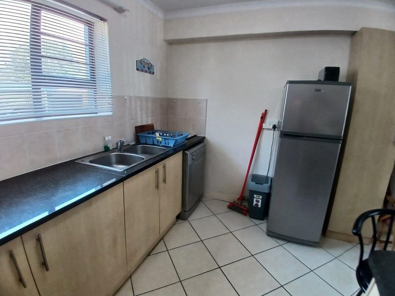 A functional kitchen featuring laminate cabinetry, a double bowl stainless steel sink, tiled splashbacks, and tiled flooring with a window providing natural light.