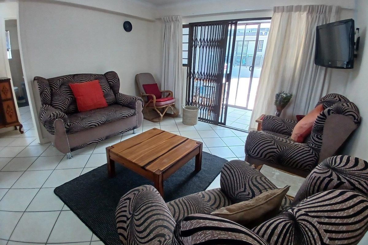 A living room featuring ceramic floor tiles and a sliding glass door with a security gate, providing access to an outdoor area.