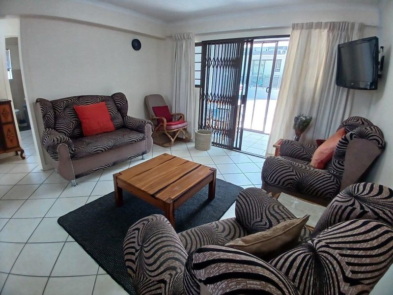A living room featuring ceramic floor tiles and a sliding glass door with a security gate, providing access to an outdoor area.
