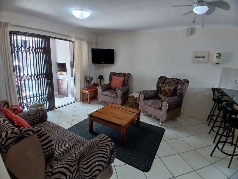 Open plan living area featuring tiled flooring, a ceiling fan, and a sliding door leading to a patio with a built-in braai.