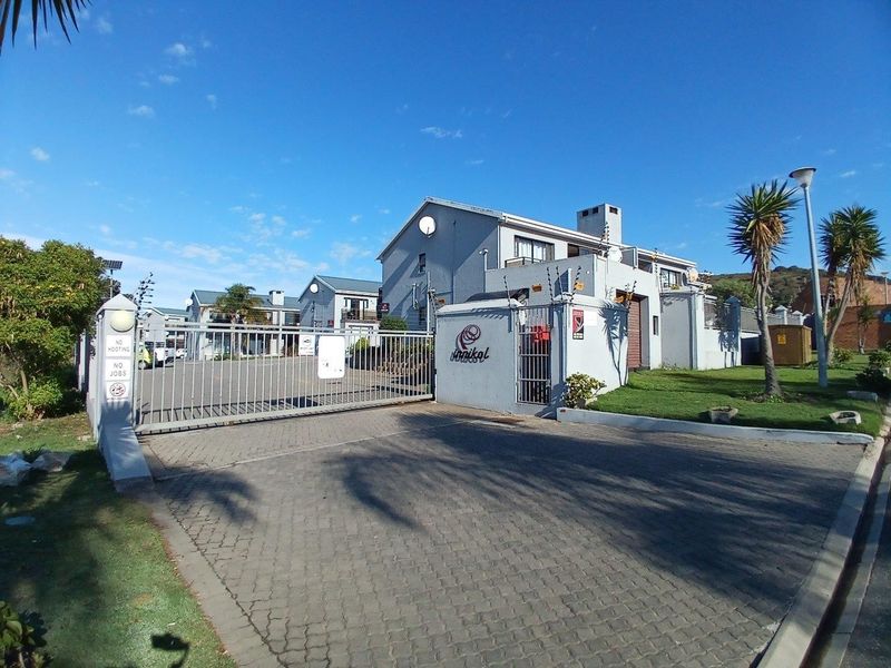 Front entrance view of the apartment complex featuring a paved driveway, secure electric gate, and perimeter wall with electric fencing.