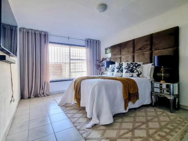 A well-maintained bedroom featuring tiled flooring, large window with blinds, and neutral wall finishes, providing a comfortable and functional living space.