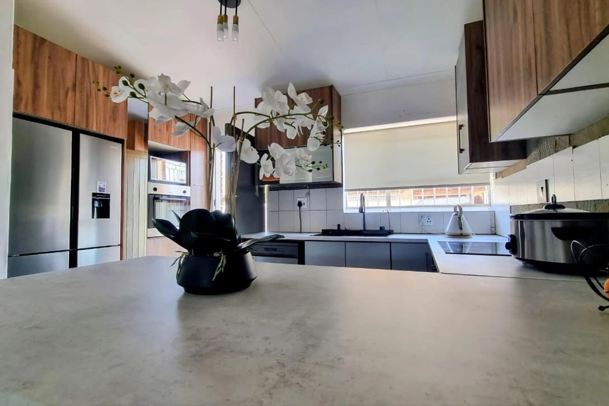 Modern kitchen featuring wood-finish cabinetry, stone-look countertops, built-in oven, hob, and a functional tiled backsplash with ample workspace.
