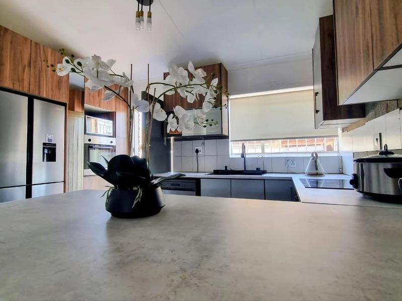 Modern kitchen featuring wood-finish cabinetry, stone-look countertops, built-in oven, hob, and a functional tiled backsplash with ample workspace.