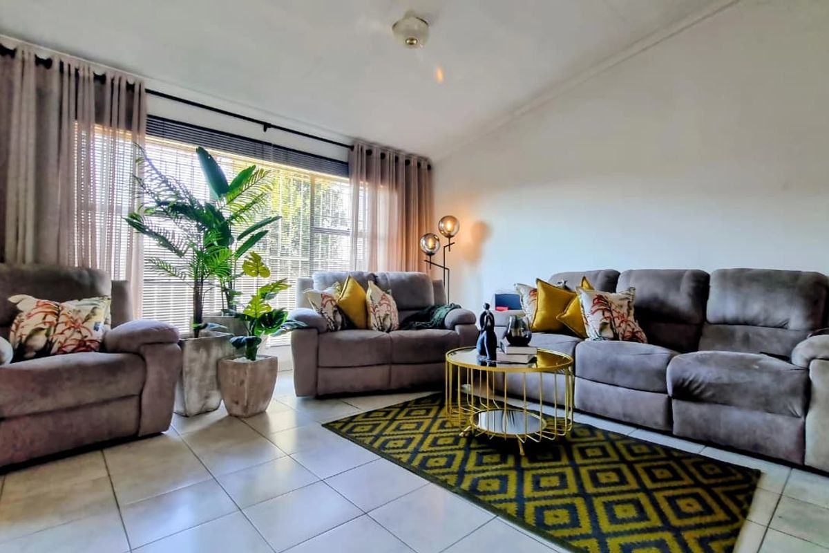 A well-lit living room featuring tiled flooring, a ceiling fan, and a large window with curtains, providing a comfortable and functional living space.