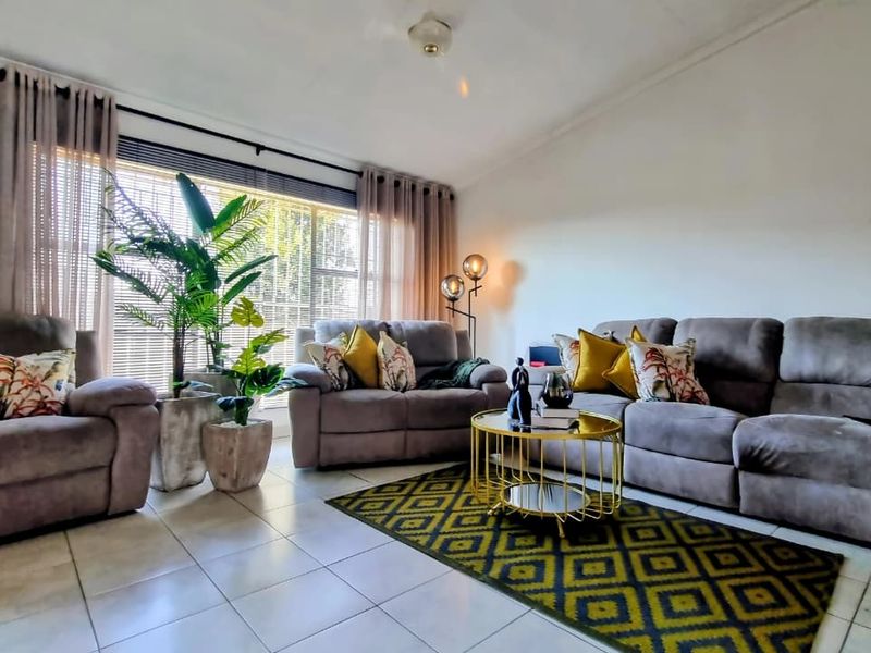 A well-lit living room featuring tiled flooring, a ceiling fan, and a large window with curtains, providing a comfortable and functional living space.