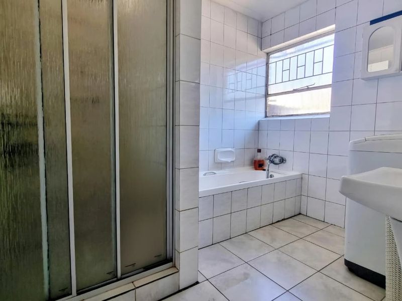 A functional bathroom featuring a built-in bathtub, separate shower enclosure, and pedestal basin, finished with white wall tiles and floor tiling.