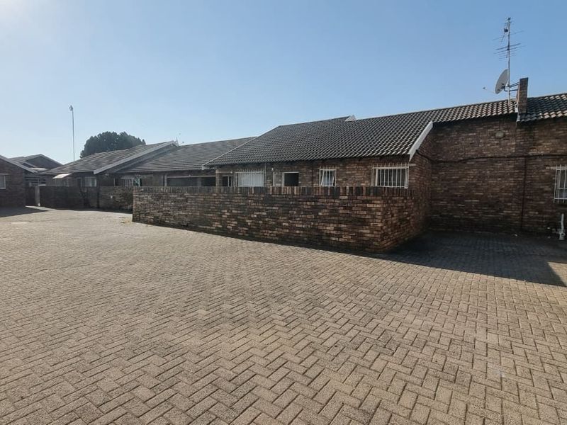 Exterior view of a townhouse complex featuring a brick facade, tiled roofing, and a spacious paved driveway area.
