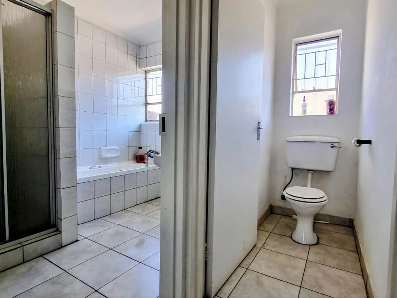 A functional bathroom featuring a separate shower enclosure, tiled bathtub, and a private toilet area with tiled finishes throughout.