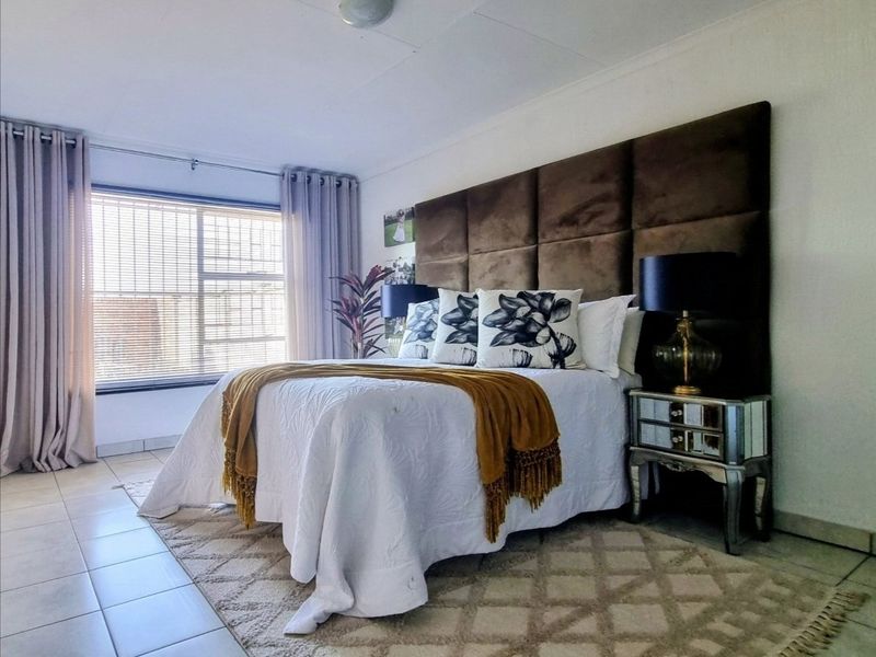 A well-maintained bedroom featuring tiled flooring, neutral wall finishes, and large windows with venetian blinds, providing a bright and comfortable living space.