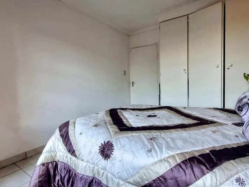 A bedroom featuring built-in cupboards and tiled flooring, requiring cosmetic updates to the wall finishes.