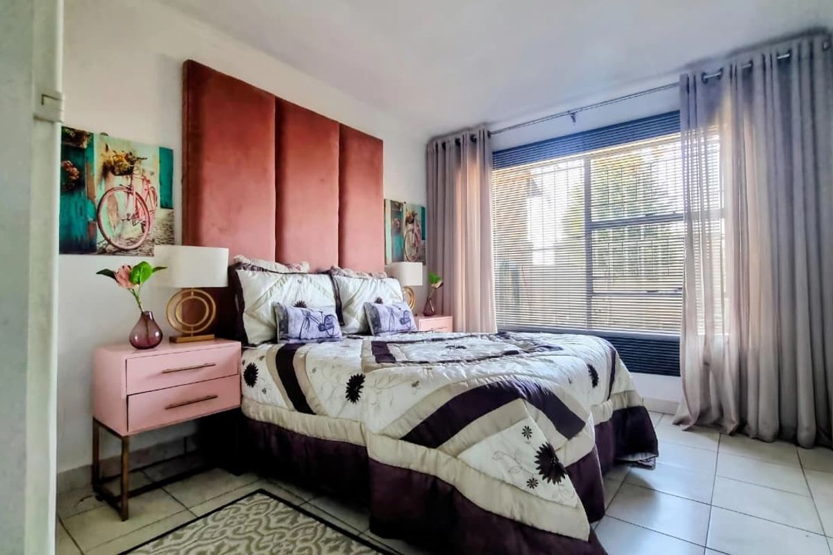 A well-lit bedroom featuring tiled flooring and large windows with fitted blinds and curtain tracks.