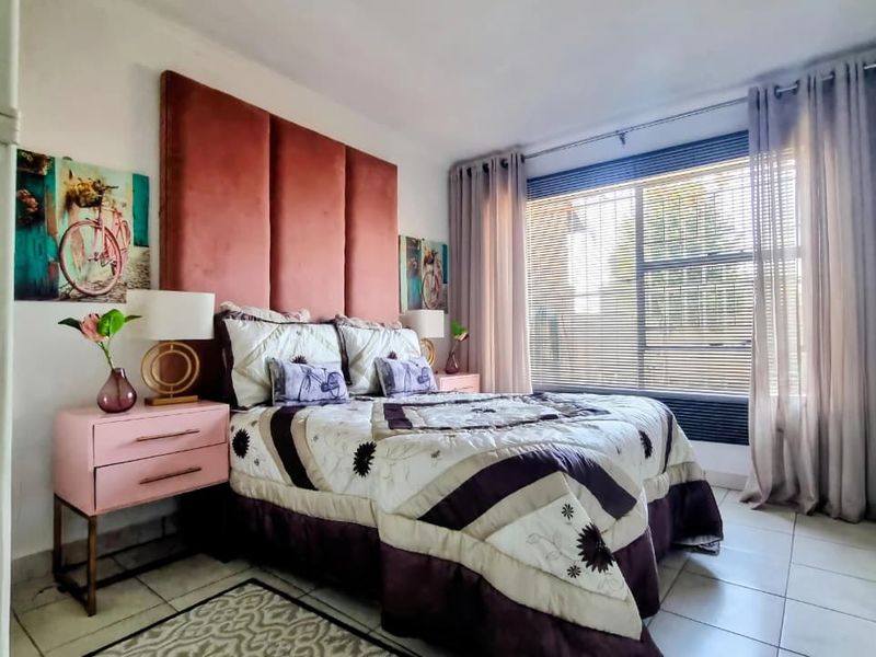 A well-lit bedroom featuring tiled flooring and large windows with fitted blinds and curtain tracks.