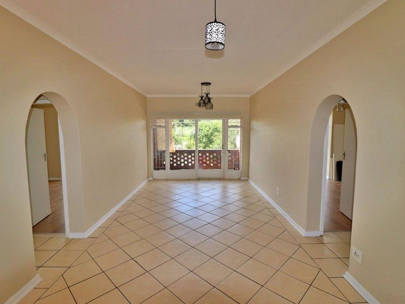 An empty living area featuring tiled floors, arched doorways leading to adjacent rooms, and sliding glass doors providing access to an outdoor space.