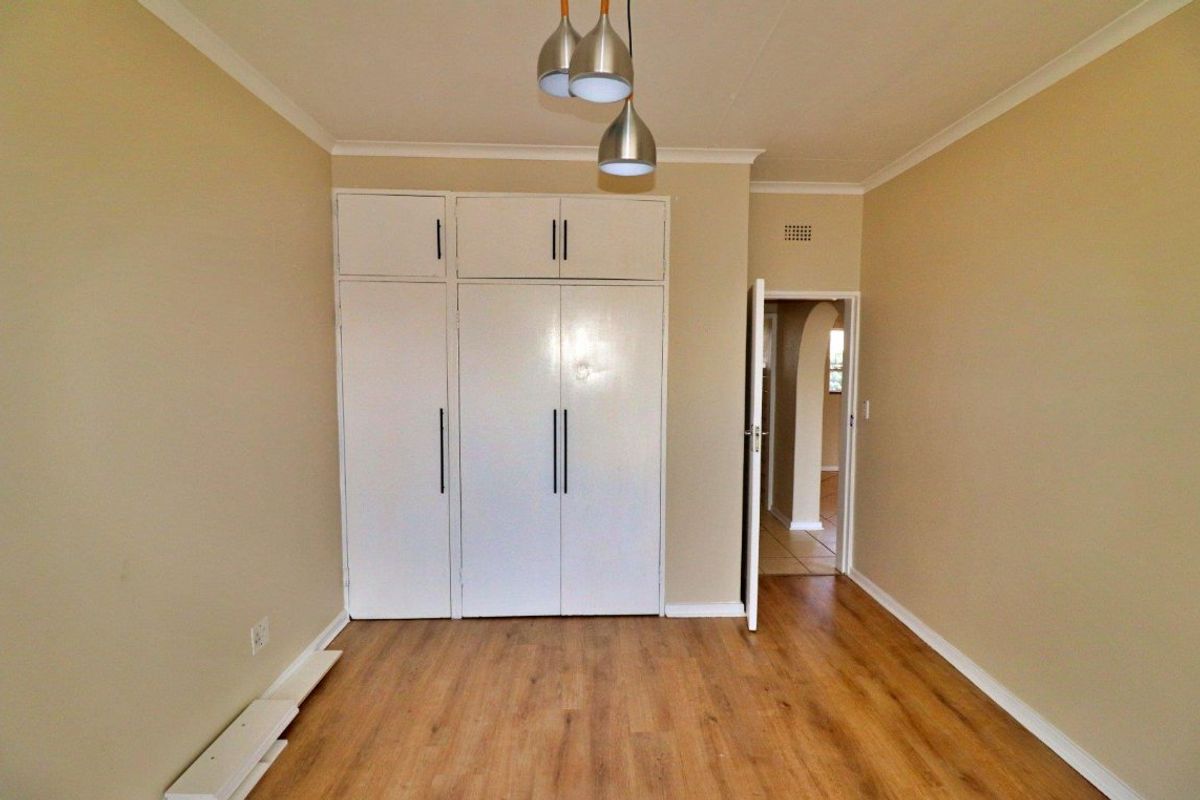 A clean, empty bedroom featuring laminate flooring, built-in cupboards, and a neutral color palette, ready for personalization.