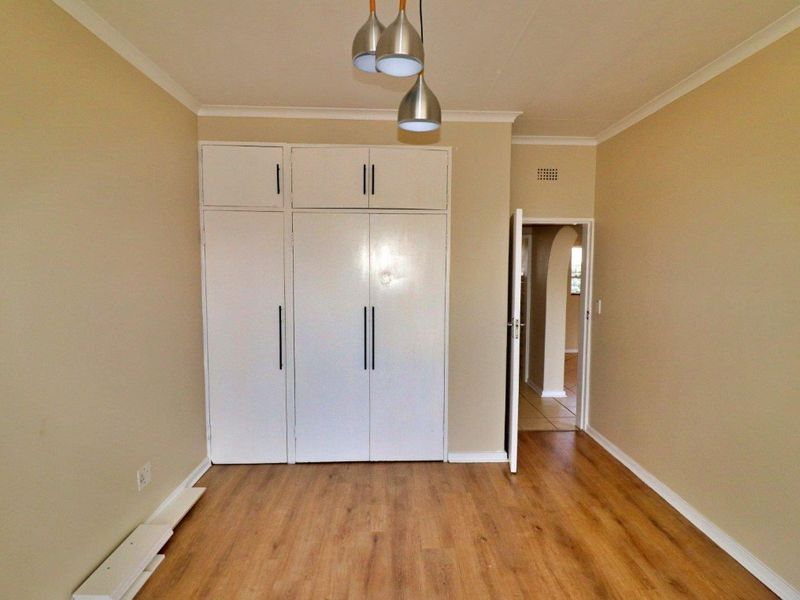 A clean, empty bedroom featuring laminate flooring, built-in cupboards, and a neutral color palette, ready for personalization.