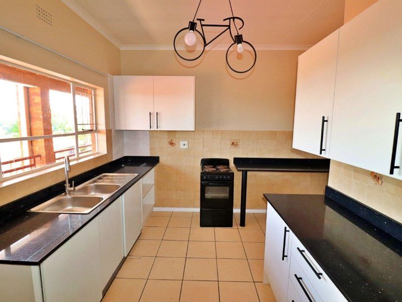 A functional kitchen featuring white cabinetry, black granite countertops, a double stainless steel sink, and tiled flooring with a neutral backsplash.