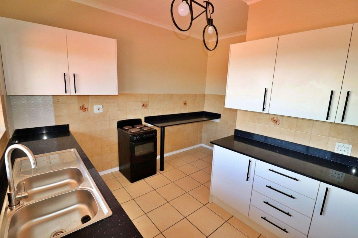 A functional kitchen featuring white cabinetry, black granite countertops, a double bowl stainless steel sink, and a freestanding stove with tiled backsplash.