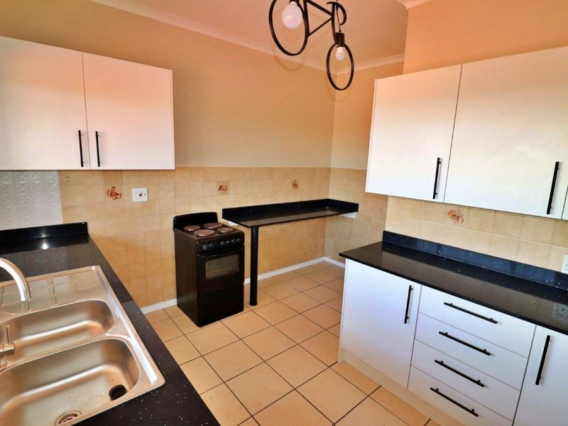 A functional kitchen featuring white cabinetry, black granite countertops, a double bowl stainless steel sink, and a freestanding stove with tiled backsplash.