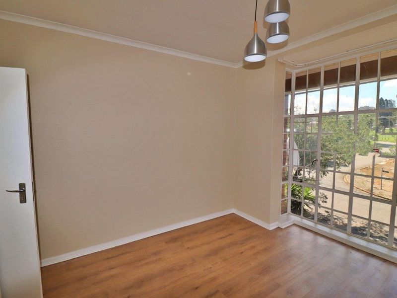 A bright, empty bedroom featuring laminate flooring, a built-in cupboard, and a large bay window providing natural light.